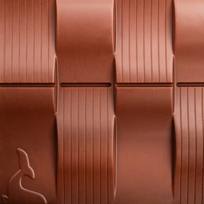 Tablette Chocolat au lait 50% de cacao de La Baleine à cabosse dans son emballage, posée à côté d'une tablette de chocolat au lai sans emballage