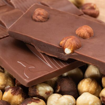 Tablette de chocolat au lait 50% de cacao & noisettes torréfiées de La Baleine à Cabosse dans son emballage, posée à côté d'un moule en forme de tablette rempli de noisettes entières