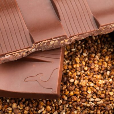 Tablette de chocolat au lait 50% de cacao & sarrasin grillé de La Baleine à Cabosse dans son emballage, posée à côté d'un moule en forme de tablette rempli de sarrasin grillé