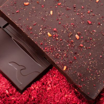 Tablette de chocolat noir 70% & framboise séchée de La Baleine à Cabosse dans son emballage, posée à côté d'un moule en forme de tablette rempli de framboise séchée en poudre