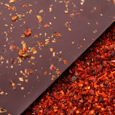 Tablette de chocolat noir 76% & piment d'Alep de La Baleine à Cabosse dans son emballage, posée à côté d'un moule en forme de tablette rempli de piment d'Alep séché