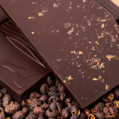 Tablette de chocolat noir 76% & poivre de timut de La Baleine à Cabosse dans son emballage, posée à côté d'un moule en forme de tablette rempli de grains de poivre de timut