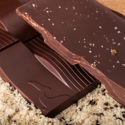 Chocolatier à Marseille - Chocolaterie artisanale La Baleine à cabosse 18 Tablette de chocolat noir 76% & sel vanillé de Mayotte de La Baleine à Cabosse dans son emballage, posée à côté d'un moule en forme de tablette rempli de sel vanillé