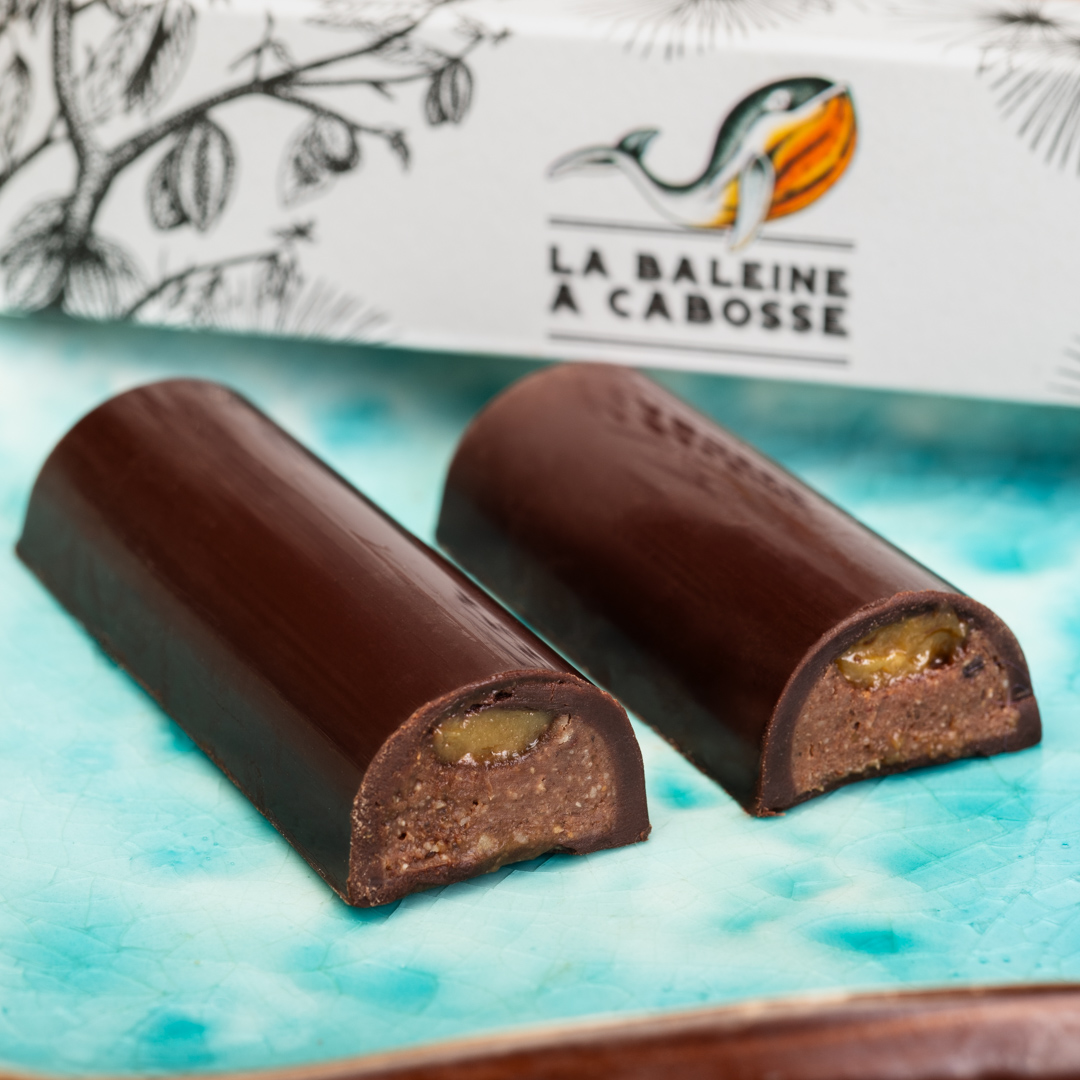 Barre fourrée praliné & caramel beurre salé 1 Barre fourrée praliné caramel beurre salé coupée en deux et posée à côté de son emballage