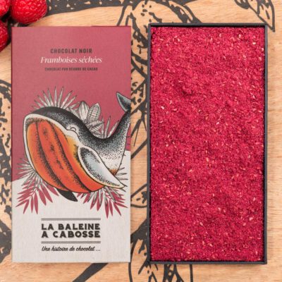 Tablette de chocolat noir 70% & framboise séchée de La Baleine à Cabosse dans son emballage, posée à côté d'un moule en forme de tablette rempli de framboise séchée en poudre