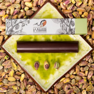 Barre fourrée au praliné de pistaches, posée à côté de son emballage sur une assiette verte, avec des pistaches tout autour