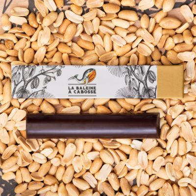 La Barre fourrée au praliné de cacahuètes sans emballage, posée à côté de l'emballage avec des cacahuètes tout autour