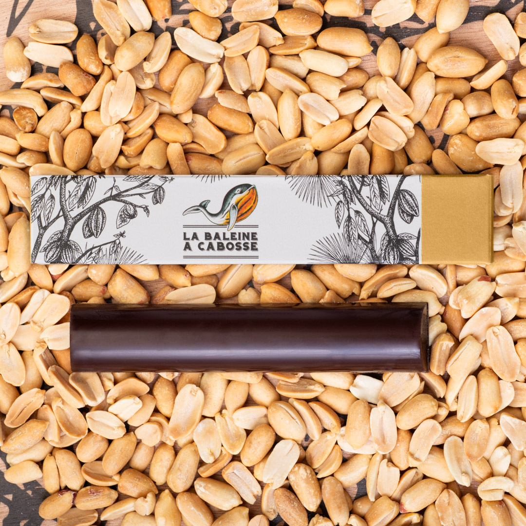 La Barre fourrée au praliné de cacahuètes sans emballage, posée à côté de l'emballage avec des cacahuètes tout autour