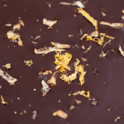 la tablette de chocolat noir aux zestes de citrons de La Baleine à Cabosse dans son emballage, posée à côté d’un moule en forme de tablette rempli de zestes de citron avec une rondelle de citron au milieu
