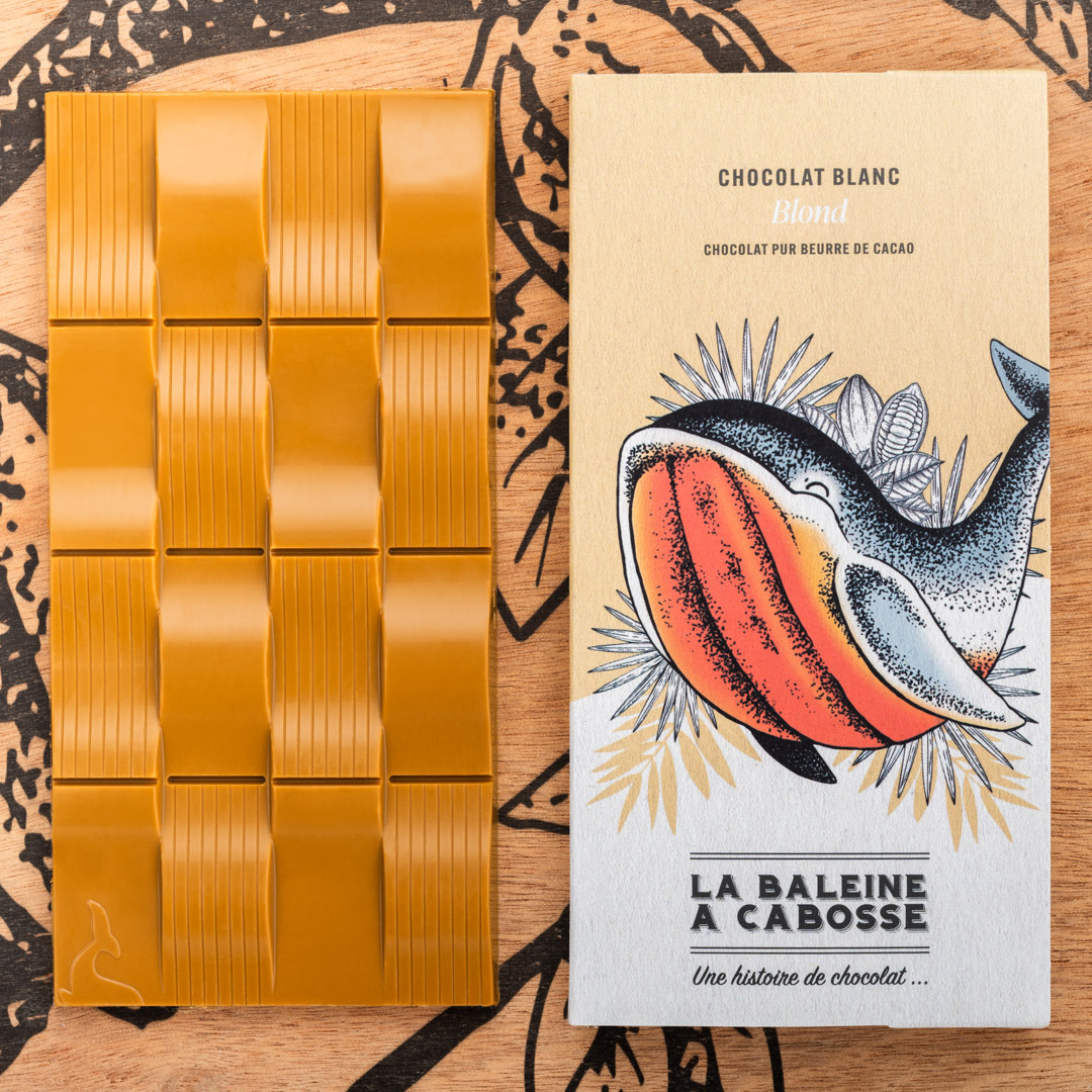Tablette Chocolat blond 1 tablette de chocolat blond de La Baleine à Cabosse dans son emballage, posée à côté de la tablette de chocolat blond sans emballage