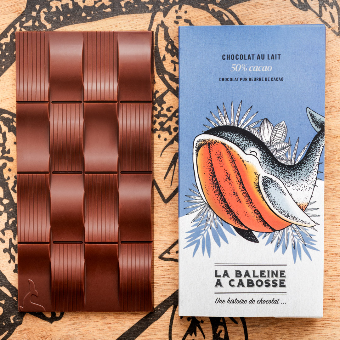 Tablette Chocolat au lait 50% de cacao 1 Tablette Chocolat au lait 50% de cacao de La Baleine à cabosse dans son emballage, posée à côté d'une tablette de chocolat au lai sans emballage