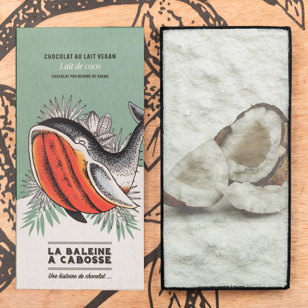 Tablette de chocolat au lait de coco 45% de cacao, vegan 1 Tablette de chocolat au lait de coco 45% de cacao de La Baleine à Cabosse dans son emballage, posée à côté d'un moule en forme de tablette avec un visuel de la noix de coco
