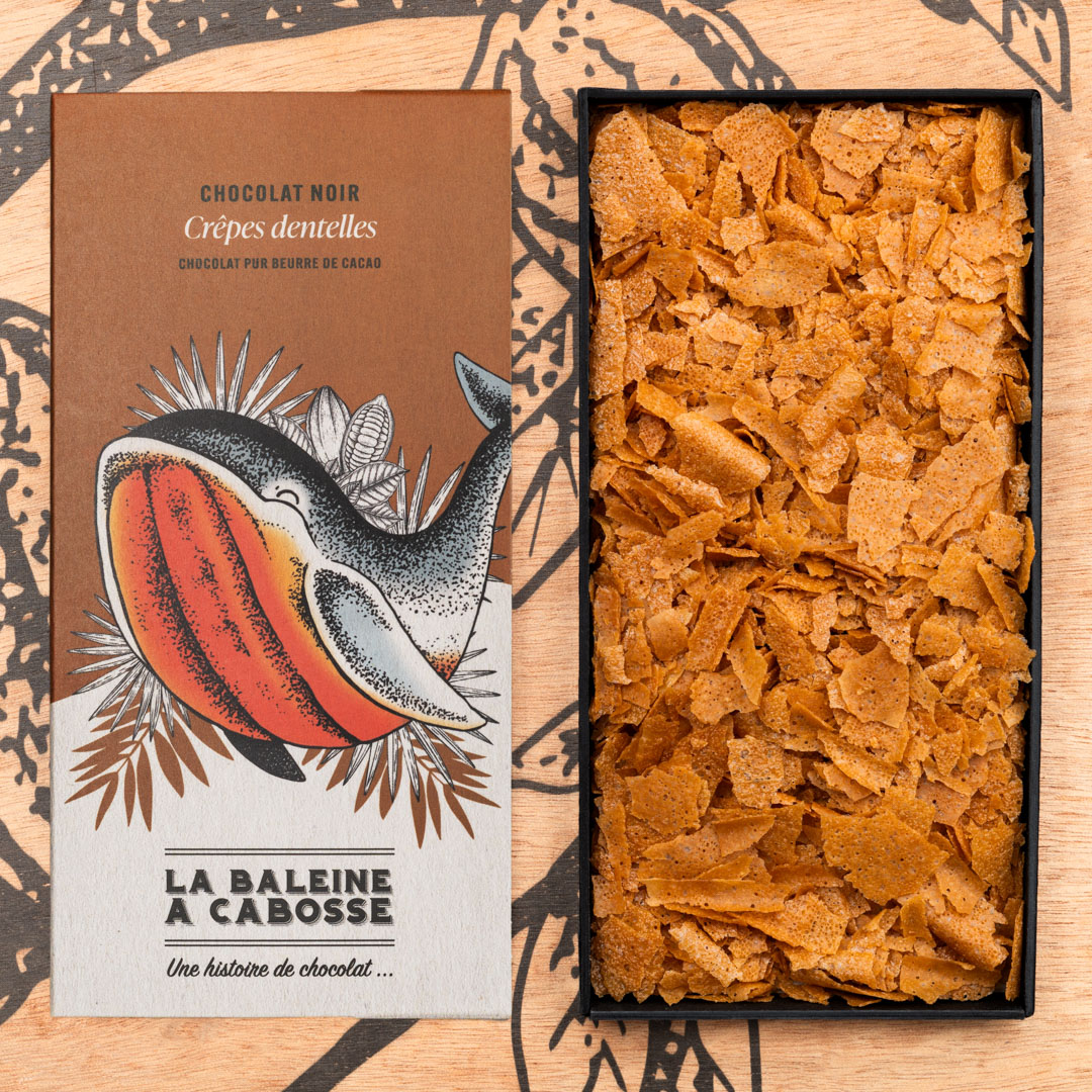 Tablette de chocolat noir 65% & crêpes dentelle 1 Tablette de chocolat noir 65% & crêpes dentelle de La Baleine à Cabosse dans son emballage, posée à côté d'un moule en forme de tablette rempli de crêpes dentelle